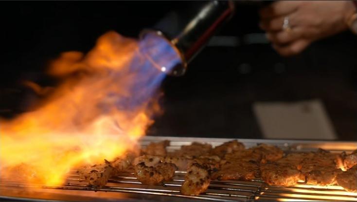 Butane culinary torch searing meat on a grill